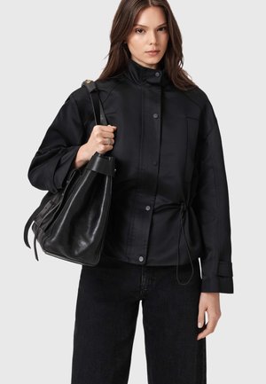 Czarna, oversize'owa kurtka z wysokim kołnierzem, zatrzaskami na zatrzaski i regulowanym sznurkiem. W połączeniu ze strukturalną czarną skórzaną torbą.
