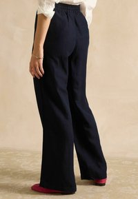 Tumesinised laia säärega püksid elastse vöökohaga, siledast kangast ja sirget lõiget, kombineeritud roosade ballerina-kingadega. Esitatud tagantvaade.