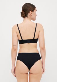 Sort bh og højtaljede trusser, sømløst design, blødt stof, justerbare stropper, minimal detaljer, set fra bagsiden.