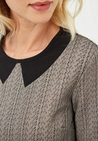 Top de patrones en negro y gris con una tela texturizada y rayas verticales, y un cuello negro en contraste.