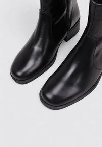 Black leather ankle boots with a smooth finish, square toes, and a low block heel. Features a side zipper for easy wear.