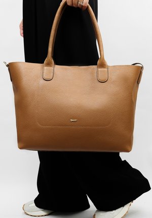 Bruine leren tote bag met een gestructureerd oppervlak, dubbele handvatten en een subtiele gouden logodetail aan de voorkant, met een ruim ontwerp.