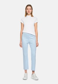 White polo shirt with short sleeves, light blue tailored pants, and white sneakers with gold accents, featuring a smooth texture and fitted design.