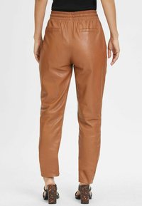 Bruine leren broek met een elastische tailleband, voorzien van achterzakken en een taps toelopend ontwerp. Soepele textuur met een subtiele glans.