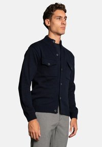 Navy button-up cardigan with a ribbed collar and cuffs, featuring two chest pockets and a textured knit pattern.