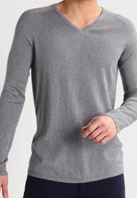 Chemise grise à manches longues avec col en V, fabriquée dans un textile doux, coupe ajustée et épaules sans coutures. Adaptée pour superposer ou porter de manière décontractée.