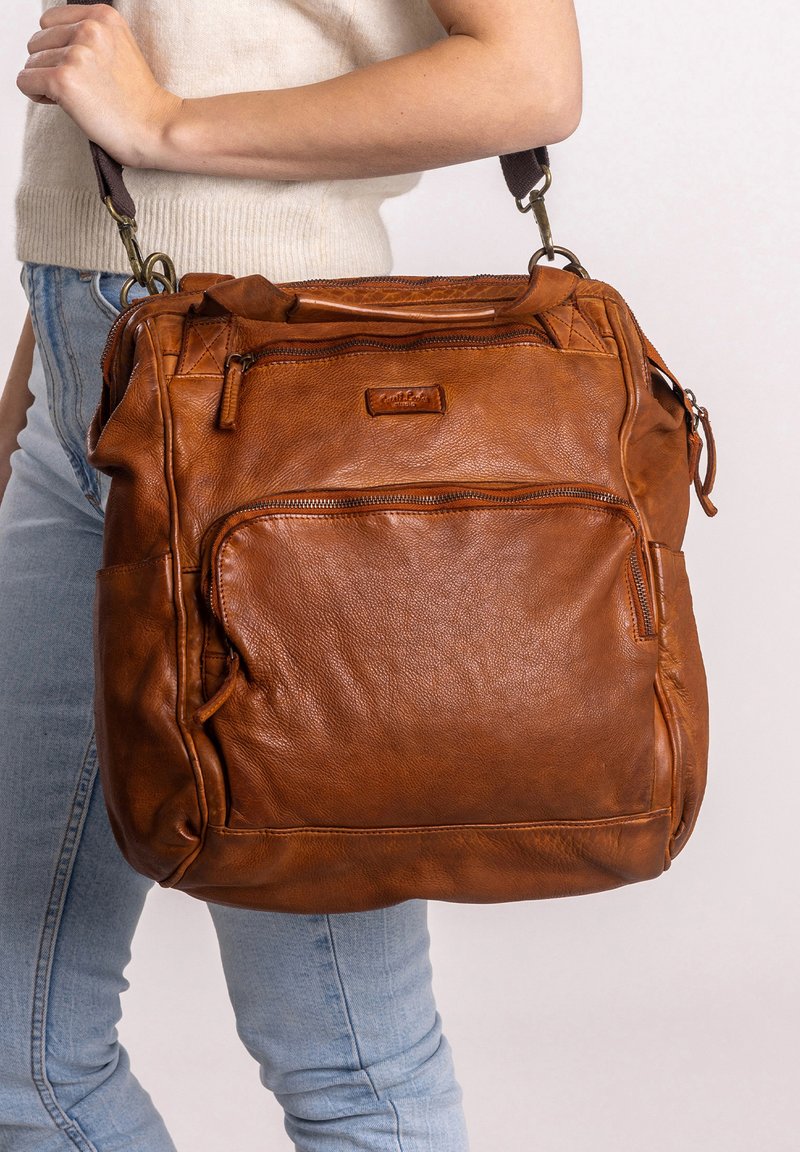 Bolso de mano de cuero marrón con un acabado texturizado, que cuenta con múltiples bolsillos con cremallera y una correa desmontable. Forma rectangular con un diseño robusto.