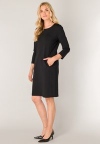 Zwarte jurk tot op de knie met driekwartmouwen, ronde halslijn en zijzakken. Heeft een gladde textuur en een minimalistisch ontwerp.