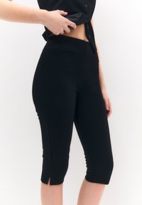 Pantaloni capri neri realizzati in tessuto elastico, con una vestibilità slim, fessure alla caviglia e tasche frontali. Progettati per un look su misura.