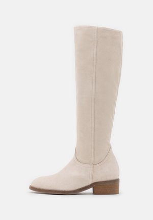 Botte beige en daim montant jusqu'au genou, avec un petit talon bloc en bois et un bout rond, vue de côté sur fond blanc.