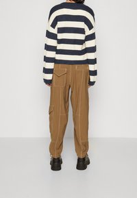 Randig tröja i marinblå och vit, kraftig stickning och lös passform. Bruna cargobyxor med synlig sömnad och sidofickor. Svarta stövlar.