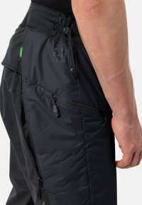 Zwarte fietspants van een geprofileerde stof, met ritssluitingen in de zakken en een verstelbare taille met een trekkoord. Logo-detail zichtbaar op de dij.