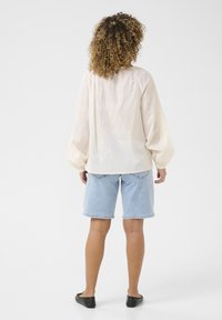 Light beige blouse with flowing balloon sleeves, and light blue denim shorts with rolled cuffs. Black flat shoes complete the outfit.