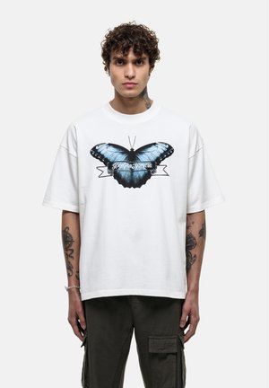 T-shirt bianca oversize con una grande grafica di una farfalla blu e la scritta "Good for Nothing" sotto il design. Maniche corte, materiale in cotone.