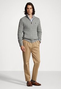 Gray cable-knit cardigan with a shawl collar, worn over a light blue shirt, paired with tan trousers and brown loafers.