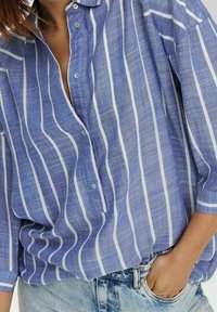 Camicia a righe blu e bianche, con bottoni, in tessuto leggero, caratterizzata da un colletto, vestibilità morbida e taschino frontale. Design testurizzato e casual.
