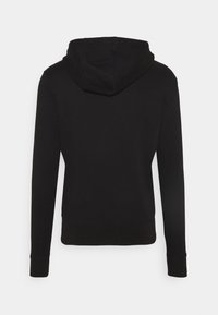 Sweat à capuche noir à manches longues, vu de dos sur un fond gris clair uni.