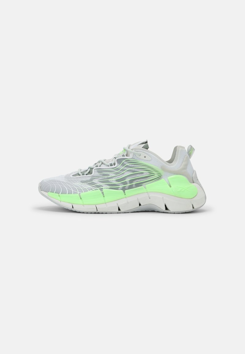 Chaussure de sport blanche et vert clair avec une semelle courbée et des motifs ondulés le long du côté, vue de l'extérieur.