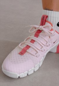 Lys rosa træningssko med mesh-overdel, kontrasterende pink detaljer, fleksibel sål og snørebåndsdesign. Hvid struktureret ydersål.