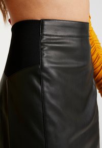 Schwarzer Kunstlederrock mit hohem Bund und einem strukturierten Strickpanel. Glatte Oberfläche mit dezenter Raffinesse und ohne sichtbare Verschlüsse.