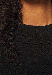 Maglione nero a coste con colletto tondo, che mostra una vista ravvicinata del tessuto testurizzato e dell'area delle spalle, arricchito da capelli texturizzati.