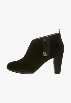 Botín de ante negro con forma curva, detalle de cremallera lateral y tacón de bloque texturizado. Presenta una correa con una hebilla decorativa.