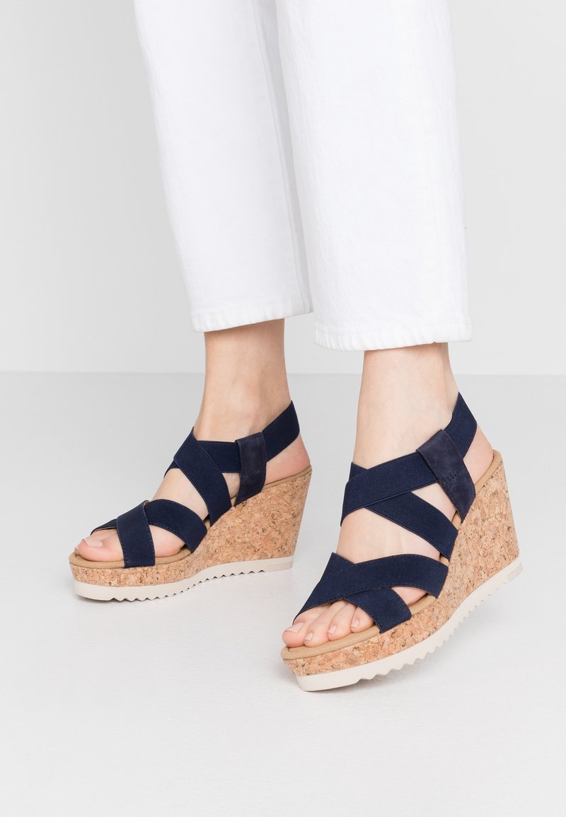 Navy wedged sandals with cork heel, elastic crisscross straps, open toe design, and rubber sole. Curved wedge adds height.