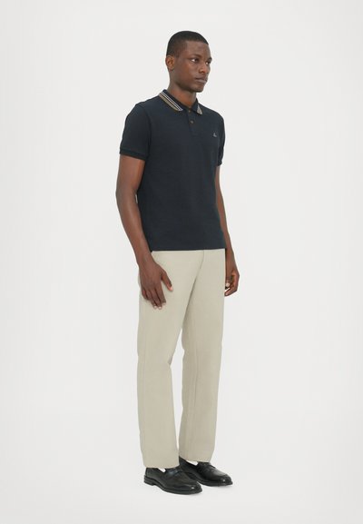 Tricou polo bleumarin cu guler, cu accente în dungi, asortat cu pantaloni bej deschis și pantofi negri. Design simplu, cu o formă ajustată.