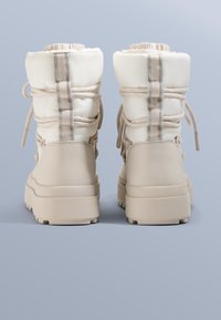 Beżowe ocieplane buty z wyściełanym cholewką, sznurowadłami do ściągania i gumową podeszwą. Charakteryzują się gładką fakturą i kontrastowym panelem z tkaniny.