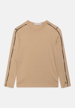 Chemise beige à manches longues avec bordure noire et marquage Calvin Klein Jeans le long des épaules et des manches, petit logo CK près du poignet.