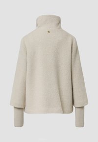 Beige trui met hoge kraag, textuurstof, losse pasvorm en geribde mouwboorden. Heeft een klein logo detail op de rug.
