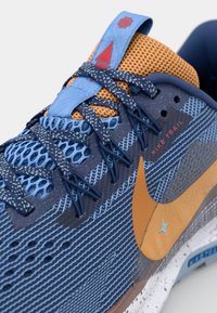 Blå og orange trail løbesko med struktureret mesh-overdel, fremtrædende snøresystem, Nike-logo og spraglet mellemsål.