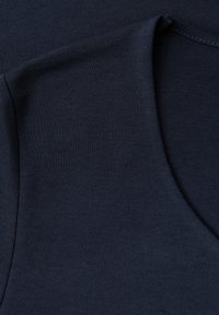 Tessuto di cotone blu navy con una texture liscia, caratterizzato da un colletto arrotondato e cuciture ben definite. Vista ravvicinata della superficie del tessuto.