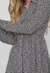 Abito floreale in bianco e nero con scollatura a colletto, maniche lunghe a sbuffo e vita arricciata, realizzato in tessuto leggero.