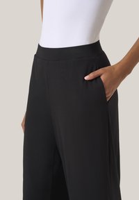 Svarta byxor med en elegant design, som har en jämn yta, bred midja och sidfickor.