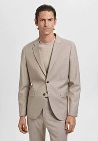 Beige tailored blazer with two front pockets, single button closure, and notch lapels, paired with a light beige knit sweater.