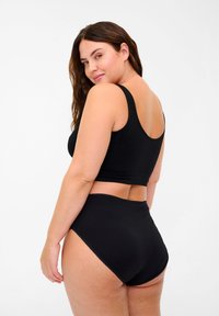 Black cotton crop top with wide straps, paired with high-waisted black briefs. The fabric is smooth, featuring subtle stitching along the edges.