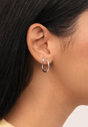 Pendientes de aro de plata con un acento de estrella, diseño elegante, acabado brillante y forma circular, llevados en el lóbulo de la oreja.