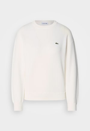 Bela dukserica izdelana iz mehke tkanine, s krožnim izrezom, dolgimi rokavi, rebrovanimi manšetami in majhnim zelenim logotipom Lacoste na prsih.