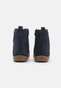 Botas de tornozelo em camurça azul-marinho com acabamento texturizado, fecho de zipper e solas de borracha bege. Apresenta um pequeno logótipo no lado exterior.