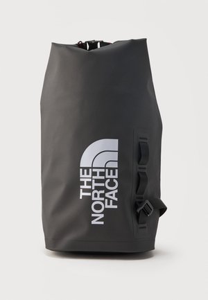 Čierny nepremokavý ruksak s rolovacím uzáverom, bielym logom The North Face a bočnými popruhmi na upevnenie výstroja.