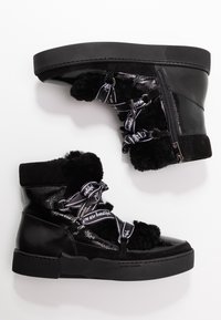 Mustat nilkkurit, joissa on kiiltävä pinta, pehmeät yksityiskohdat ja mustat nauhakiristys, joissa on tekstipainatus. Paksu pohja ja sivuvetoketjuyksityiskohta.