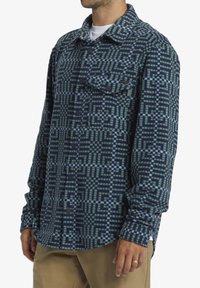 Flanellen shirt in donker marineblauw met geometrische groene en lichtblauwe patronen, met een puntige kraag, knoopsluiting aan de voorkant en borstzakken.