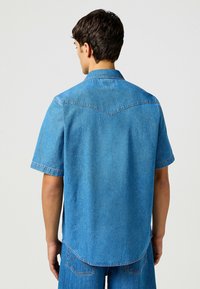 Korte mouwen denim shirt in lichtblauw, met een puntige kraag, yoke ontwerp en zichtbare stiksels. Casual pasvorm met een gebogen zoom.