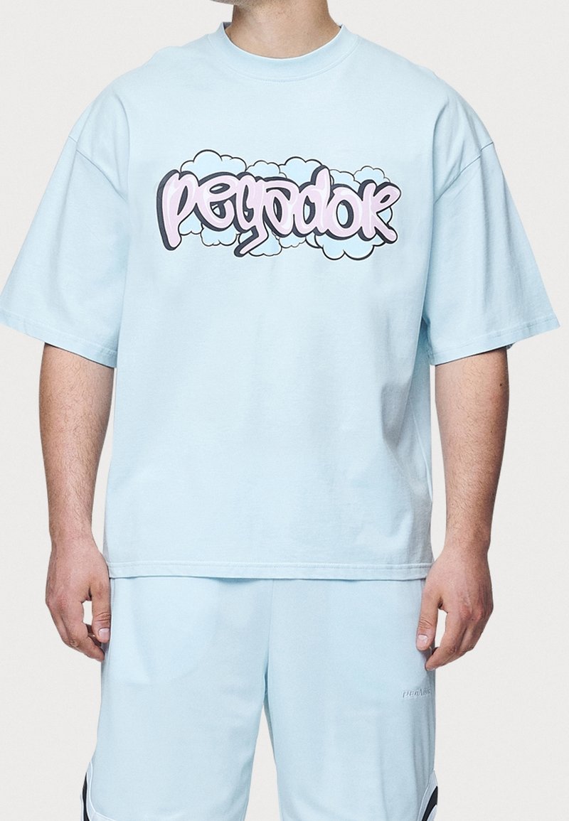 Personne portant un t-shirt oversize bleu clair avec le texte « polygodok » en style graffiti et un fond de nuages sur la poitrine, assorti à un short.