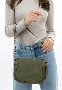 Sac bandoulière en suede vert avec des coutures contrastantes plus claires, de forme rectangulaire et des accessoires en métal fixés à la sangle.