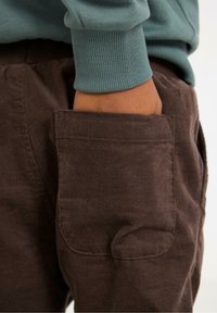 Brune fløjl bukser med en sidelomme, parret med en lyseblå sweatshirt med ribbede manchetter. Fokuser på tekstur og farvekontrast.