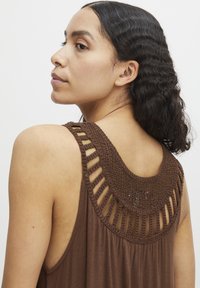 Haut sans manches marron avec un yoke texturé en crochet et des découpes verticales. Tissu doux avec une coupe décontractée et un léger tombé.
