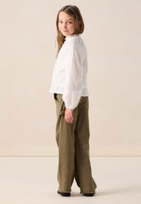 White long-sleeve blouse with textured fabric and a ruffled neckline, paired with olive green wide-leg pants featuring cargo pockets.