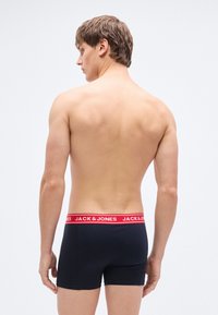 Μαύρα μπόξερ με κόκκινη ελαστική μέση που φέρει το λογότυπο "JACK & JONES". Λείο ύφασμα, εφαρμοστή σχεδίαση, μήκος μέχρι το μέσο του μηρού.
